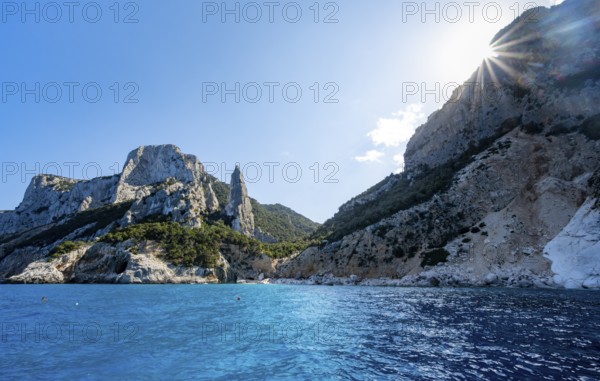 Picturesque rocky coast, cliffs with L'Aguglia pinnacle, blue sea and Cala Goloritzé beach, sun star, Golfo di Orosei, Baunei, Sardinia, Italy