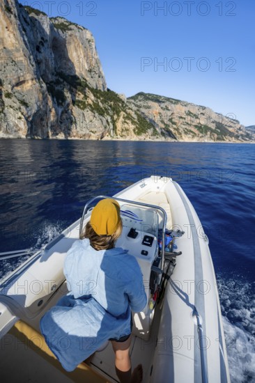 Young woman riding a motorboat along the picturesque rocky coast, cliffs and blue sea, Golfo di Orosei, Baunei, Sardinia, Italy