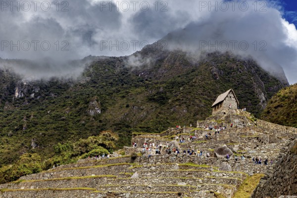 Stone structures on steep terraces in front of a cloudy mountain, The ruins of the Inca city of Machu Picchu in Peru