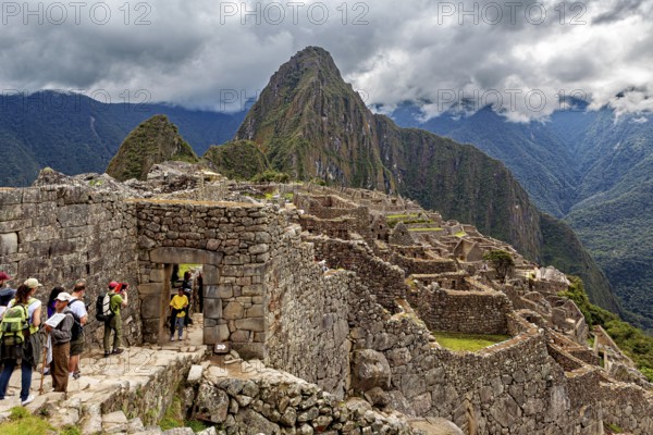 Visitors enter the ancient ruins of Machu Picchu under cloudy skies, The ruins of the Inca city of Machu Picchu in Peru