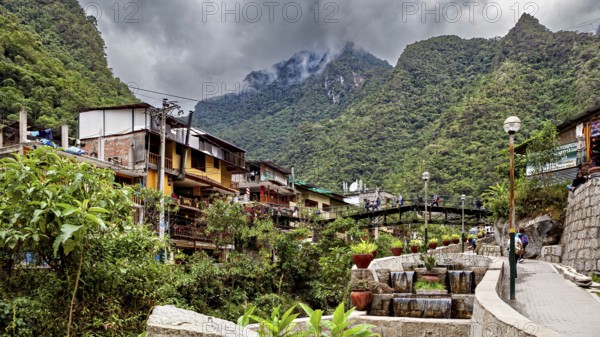 Small village surrounded by mountains under cloudy skies with lush vegetation, The city in the Urubamaba Valley near Machu Picchu in Peru