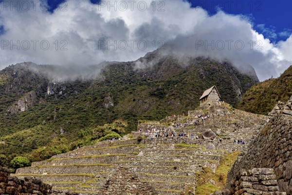 Ancient stone structures on green terraces under a cloudy sky, the ruins of the Inca city of Machu Picchu in Peru