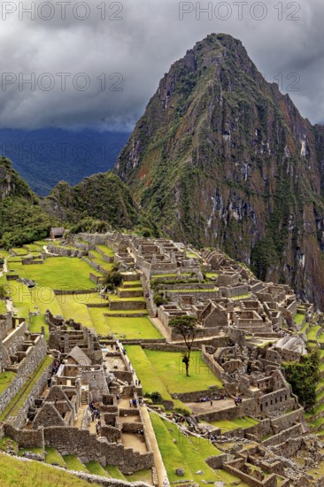 Historic ruins and a dramatic mountain against a cloudy sky, The ruins of the Inca city of Machu Picchu in Peru