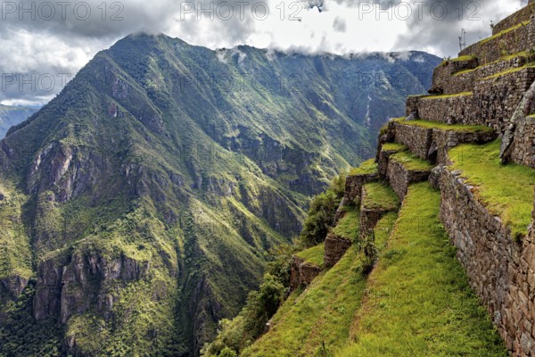 Stone terraces along a slope with spectacular panoramic views of the green mountains, the ruins of the Inca city of Machu Picchu in Peru