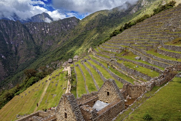 Ancient stone structures and terraces on a green mountainside under clouds, the ruins of the Inca city of Machu Picchu in Peru