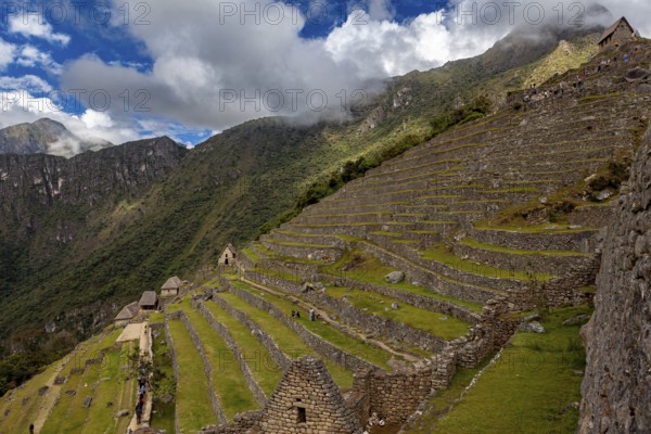 Wide view of stone terraces on a mountainside under clouds, The ruins of the Inca city of Machu Picchu in Peru