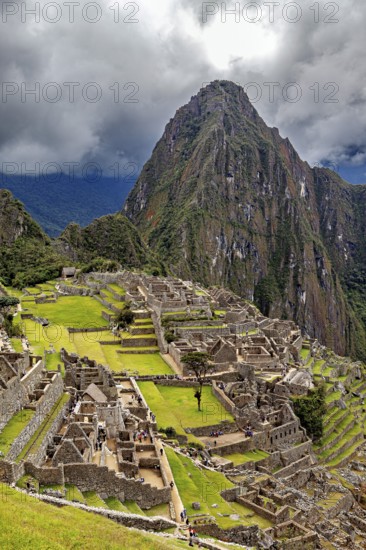 View of historic ruins and a mountain peak under a dramatic sky, The ruins of the Inca city of Machu Picchu in Peru
