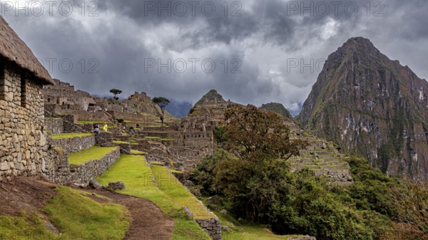 Ruins of Machu Picchu in the foreground against dramatic skies with thick clouds and green areas, The ruins of the Inca city of Machu Picchu in Peru