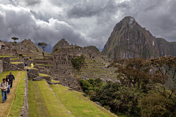 Walkers explore the ruins of Machu Picchu in front of dramatic mountain scenery, The ruins of the Inca city of Machu Picchu in Peru