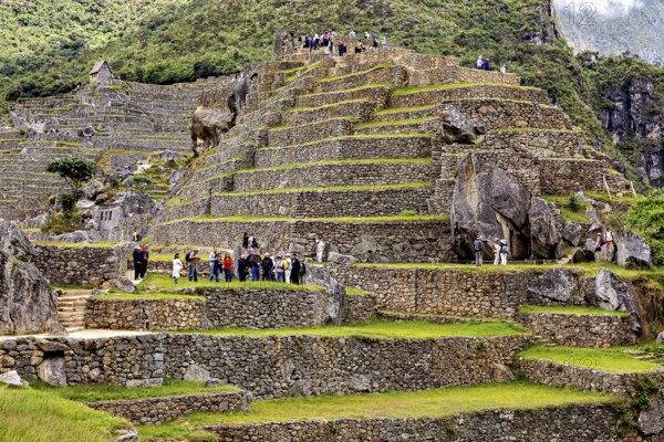 Ruins on terraces full of visitors with surrounding mountains and dramatic clouds, The ruins of the Inca city of Machu Picchu in Peru