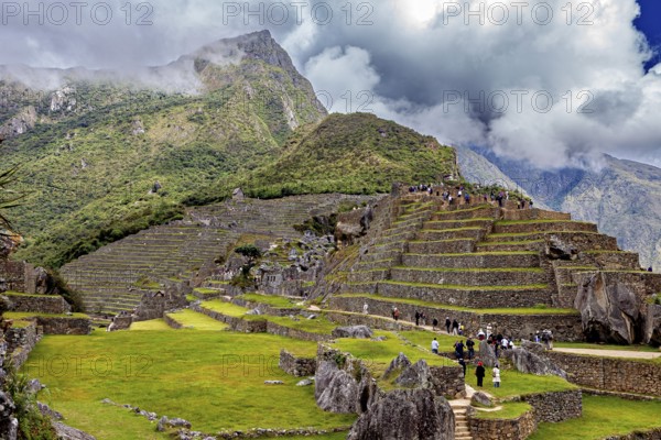 Stepped terraces with ruins against a dramatic mountain backdrop full of clouds, The ruins of the Inca city of Machu Picchu in Peru