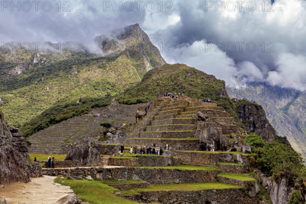 Terraces and ruins on a mountain with dramatic clouds and wandering visitors, The ruins of the Inca city of Machu Picchu in Peru