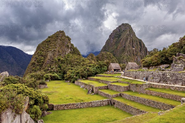Green terraces and ruins against a dramatic, cloud-covered background, the ruins of the Inca city of Machu Picchu in Peru