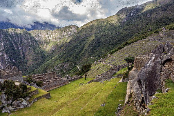 Descending terraces of ruins against mountain backdrop and cloudy sky, The ruins of the Inca city of Machu Picchu in Peru