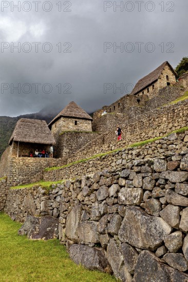 Stone walls and traditional houses against a dramatic, cloudy sky, the ruins of the Inca city of Machu Picchu in Peru