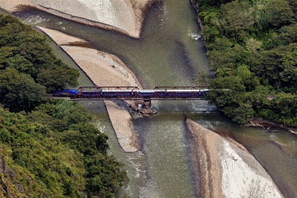 Train on a bridge over a river through a wooded landscape with sandbanks, view of the Urubamba Valley near Machu Picchu in Peru