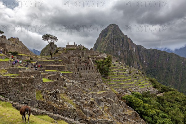Historic ruins of Machu Picchu against a cloudy mountain backdrop with tourists, The ruins of the Inca city of Machu Picchu in Peru