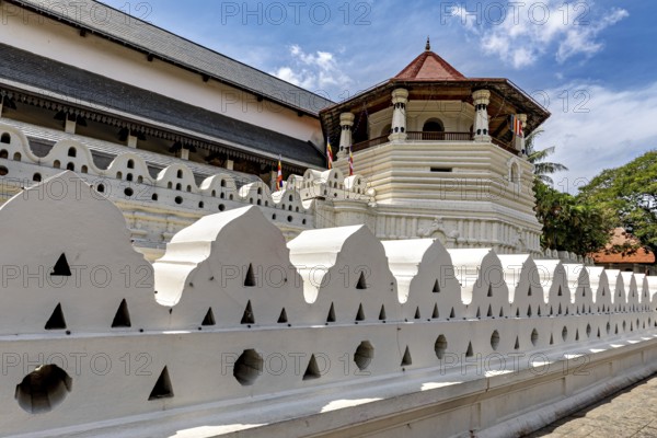 A temple with a white wall and a red roof under a clear sky, The Temple of the Tooth in Kandy Sri Lanka