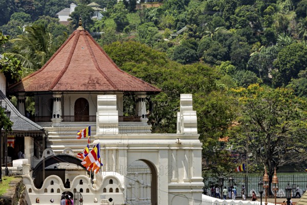 A temple with a pavilion surrounded by colorful flags and a river in the background, The Temple of the Tooth in Kandy Sri Lanka