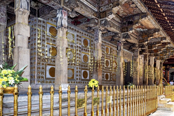 Richly decorated temple structure with ornate columns, golden ornaments and floral decorations in a religious atmosphere, the decoration inside the Temple of the Tooth of Kandy Sri Lanka