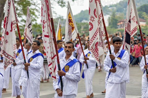 Participants wearing festive white uniforms carry red and white flags in a celebratory parade, The Perahera Parade in Kandy Sri Lanka
