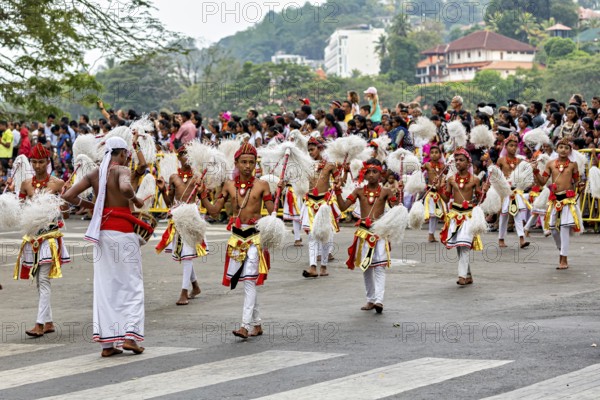 Children in festive dance costumes move happily through the streets, watched by spectators, The Perahera Parade in Kandy Sri Lanka