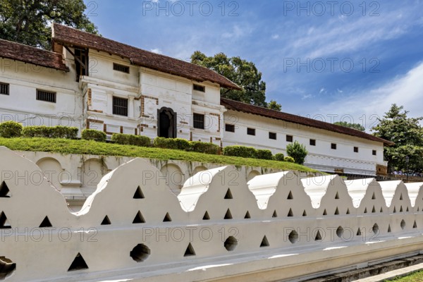 Historic temple with white stone wall, red roof and clear sky, The Temple of the Tooth in Kandy Sri Lanka