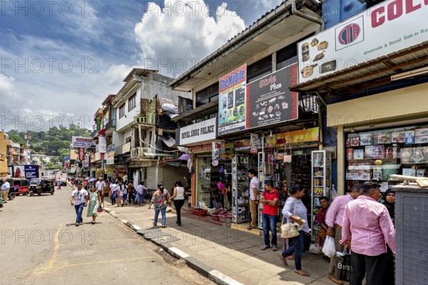 Busy shopping street with shops and passers-by under a cloudy sky in an urban setting, The shopping street in the city center of Kandy Sri Lanka
