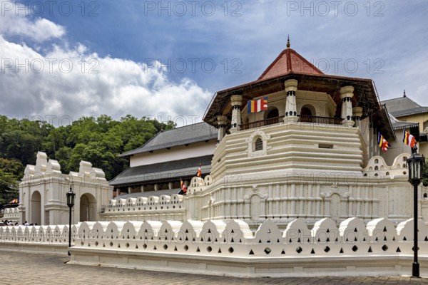 Temple complex with white wall, pavilion and colorful flags on a clear day, The Temple of the Tooth in Kandy Sri Lanka