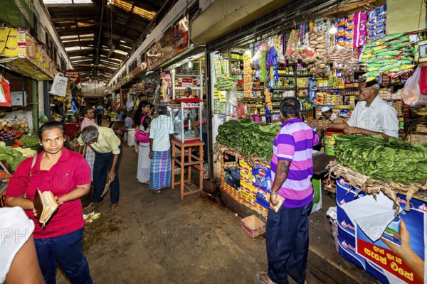 Customers move through a market aisle filled with a wide range of products, retailers in the market halls of Kandy Sri Lanka