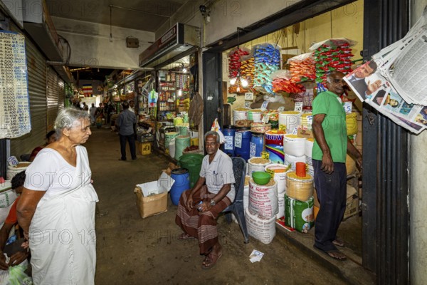 Elderly woman and salesman in a market aisle with colorful goods and packaging, dealer in the market halls of Kandy Sri Lanka