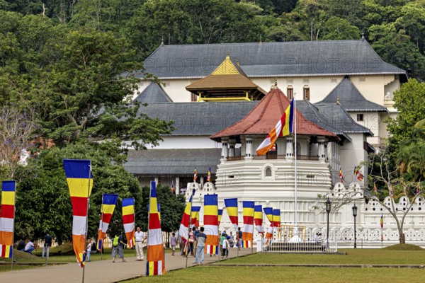 Historic building with colorful flags and group of visitors in a green setting, The Temple of the Tooth in Kandy Sri Lanka