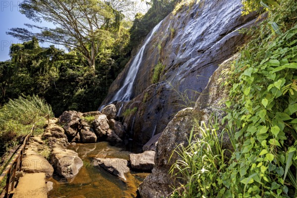 A trail leads past a large waterfall surrounded by lush greenery, waterfall in the highlands near Kandy Sri Lanka
