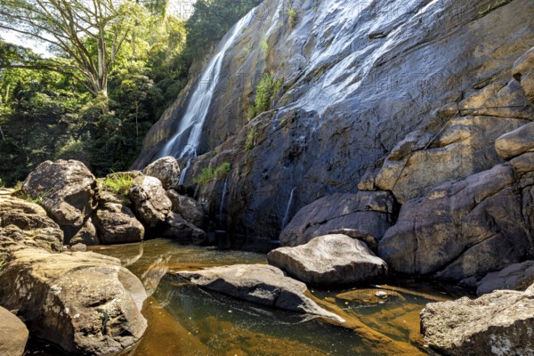 A waterfall flows over large rocks surrounded by trees, waterfall in the highlands near Kandy Sri Lanka