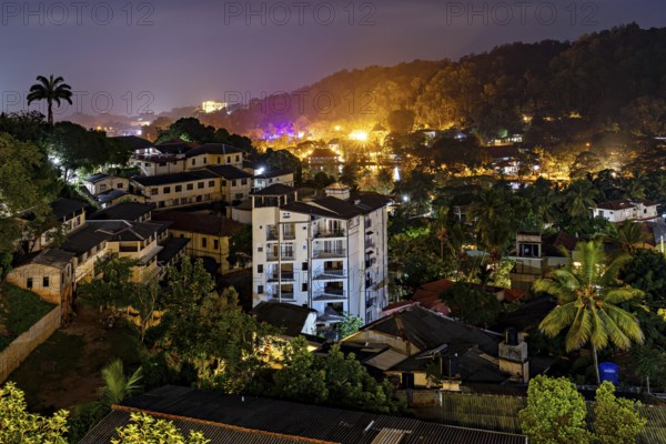 City at night with illuminated buildings and lush vegetation in hilly surroundings, conveys a lively atmosphere, view of the city of Kandy in Sri Lanka at night
