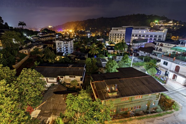 Nocturnal scene with illuminated buildings and tropical plants, conveys a lively and warm atmosphere, view of the city of Kandy in Sri Lanka at night