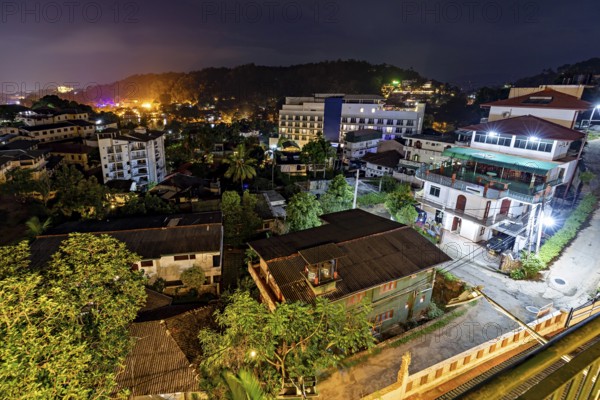 Nighttime city view with illuminated buildings and tropical trees creating a warm and inviting atmosphere, view of the city of Kandy in Sri Lanka at night