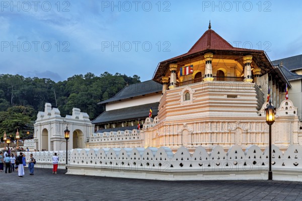 Historic building illuminated at dusk with visitors in the foreground, The Temple of the Tooth in Kandy Sri Lanka