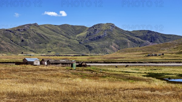 Small houses in front of a hill and mountain landscape under a blue sky, The landscape in the highlands of Peru