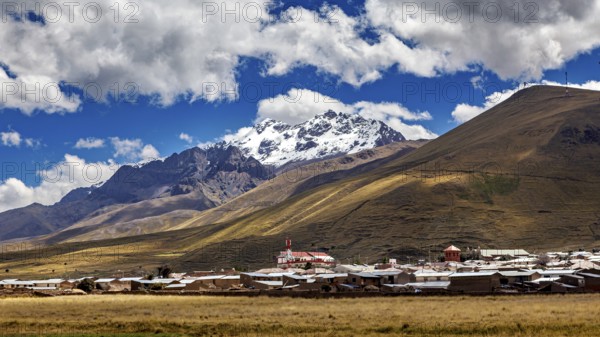 A village at the foot of snow-capped mountains under a blue sky with clouds, The countryside in the highlands of Peru