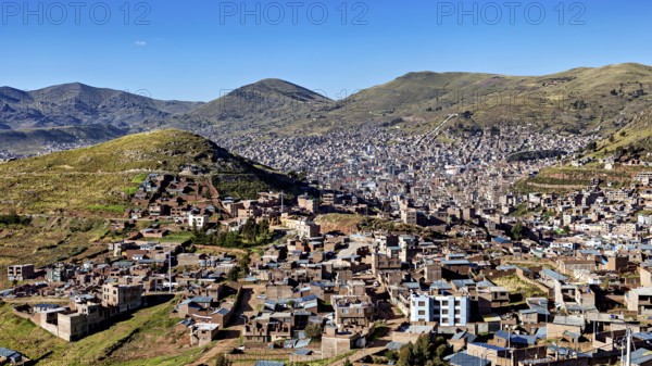 City view of buildings and mountains framed by green hills under a clear blue sky, view of the city of Puno in Peru