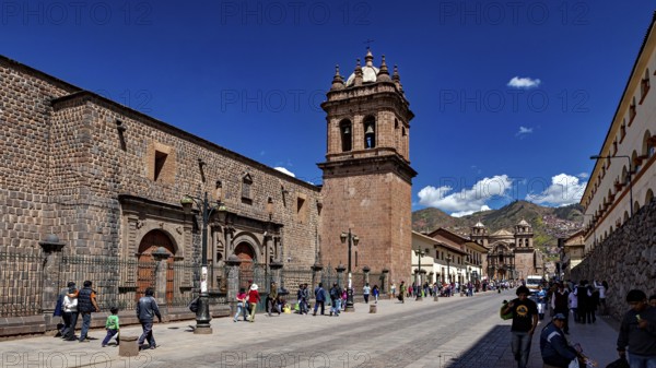 Historic street with impressive bell tower and mountain views, lively with passers-by in clear skies, The churches of Cusco in Peru