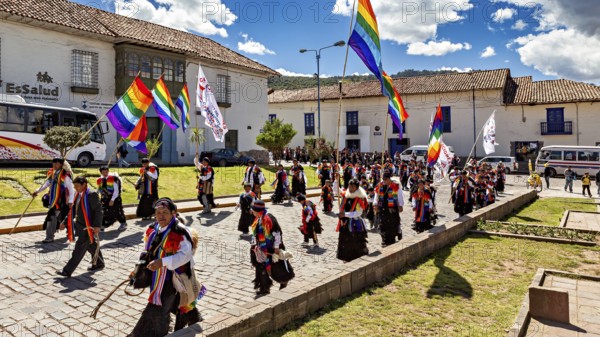 People in a colorful parade with rainbow flags walk along under a sunny sky, traditional parade of festival groups in Cusco in Peru
