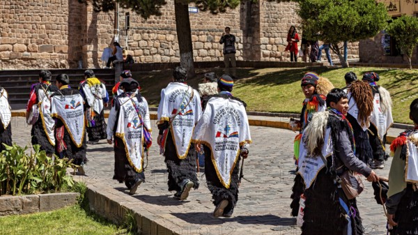 Group of people in white robes with back lettering move down the street during a procession, Traditional parade of festival groups in Cusco in Peru