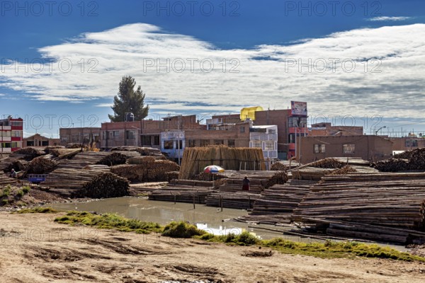 Rural cityscape with stacked wood and water surrounded by buildings under a cloudy sky, tropical timber warehouse near Puno in Peru