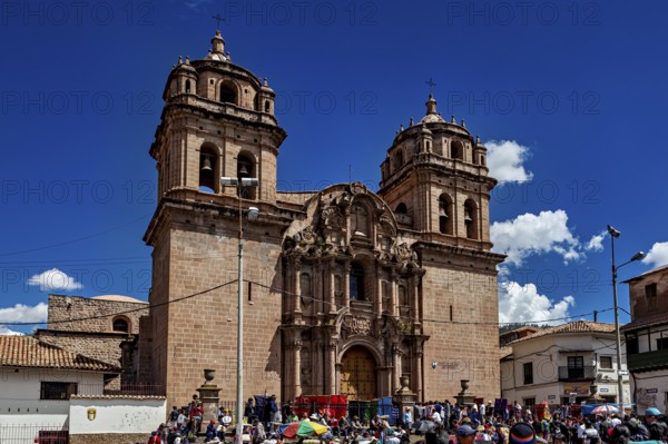 Impressive cathedral with decorated towers surrounded by a lively crowd and a clear sky, The churches of Cusco in Peru