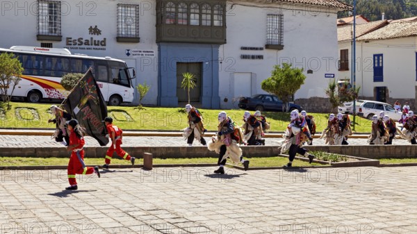 Walking people in masks and costumes cross a paved street, traditional parade of festival groups in Cusco in Peru
