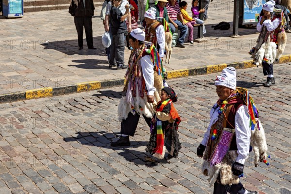People in traditional costumes, including a child, on a paved street, traditional parade of festival groups in Cusco in Peru