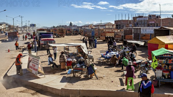 Municipal market with market stalls, people and trucks under clear blue sky, people in the streets of Puno in Peru