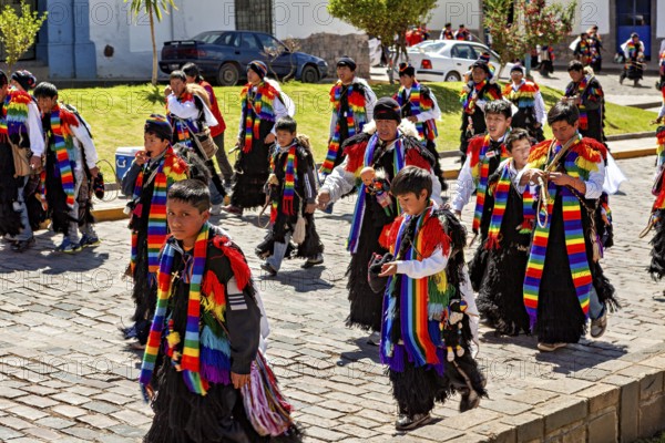 Group of people in colorful costumes walking along the street in sunny weather, traditional parade of festival groups in Cusco in Peru